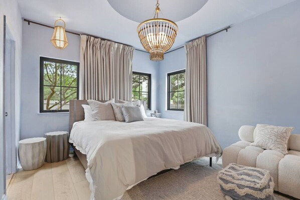 A bedroom with a large bed, two windows, a chandelier, and a sofa.