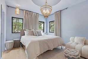 A bedroom with a large bed, two windows, a chandelier, and a sofa. - Bouldin 6 bedroom with heated pool (Austin)
