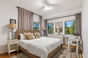 Um quarto com cama, mesas de cabeceira, cômoda, cadeira e ventilador de teto.