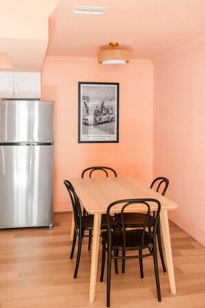 Un coin repas avec une table et des chaises en bois, un réfrigérateur en acier inoxydable et une photographie encadrée accrochée au mur.