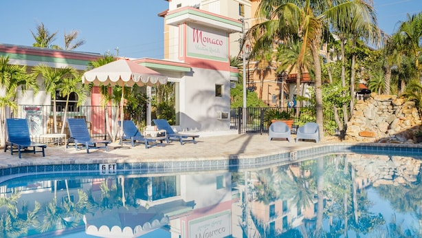 A pool area with lounge chairs, a sign for 'Monaco Vacation Rentals', and palm trees.