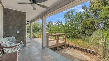 Relax in a serene outdoor space with a ceiling fan overhead, surrounded by lush greenery and a wooden deck.