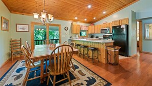 Une cuisine spacieuse avec des meubles en bois, un îlot central doté de tabourets, un réfrigérateur et un coin repas avec une grande table et des chaises.