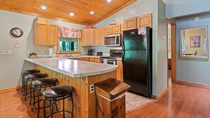 Une cuisine avec des meubles de rangement en bois, un réfrigérateur noir, un plan de travail en marbre et un coin bar avec des tabourets en bois.