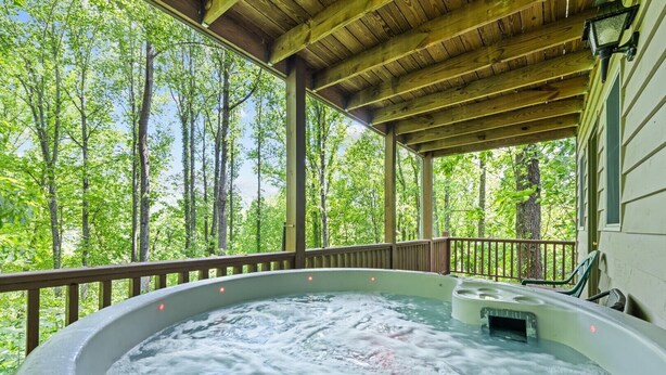 Un bain à remous installé sous une terrasse en bois, avec vue sur la forêt.