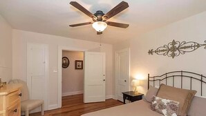 Une chambre à coucher comprenant un lit, une table de chevet, une chaise, une commode et un ventilateur de plafond.