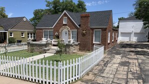 Une maison d’habitation avec une façade en briques, des fondations en pierre et une clôture en bois peinte en blanc.