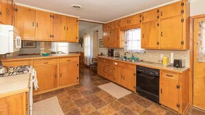 Une cuisine avec des meubles de rangement en bois, une cuisinière à gaz, un lave-vaisselle et une fenêtre avec des rideaux.