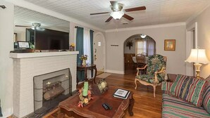 Un salon avec une cheminée, un ventilateur de plafond, un canapé, un fauteuil et une table basse.