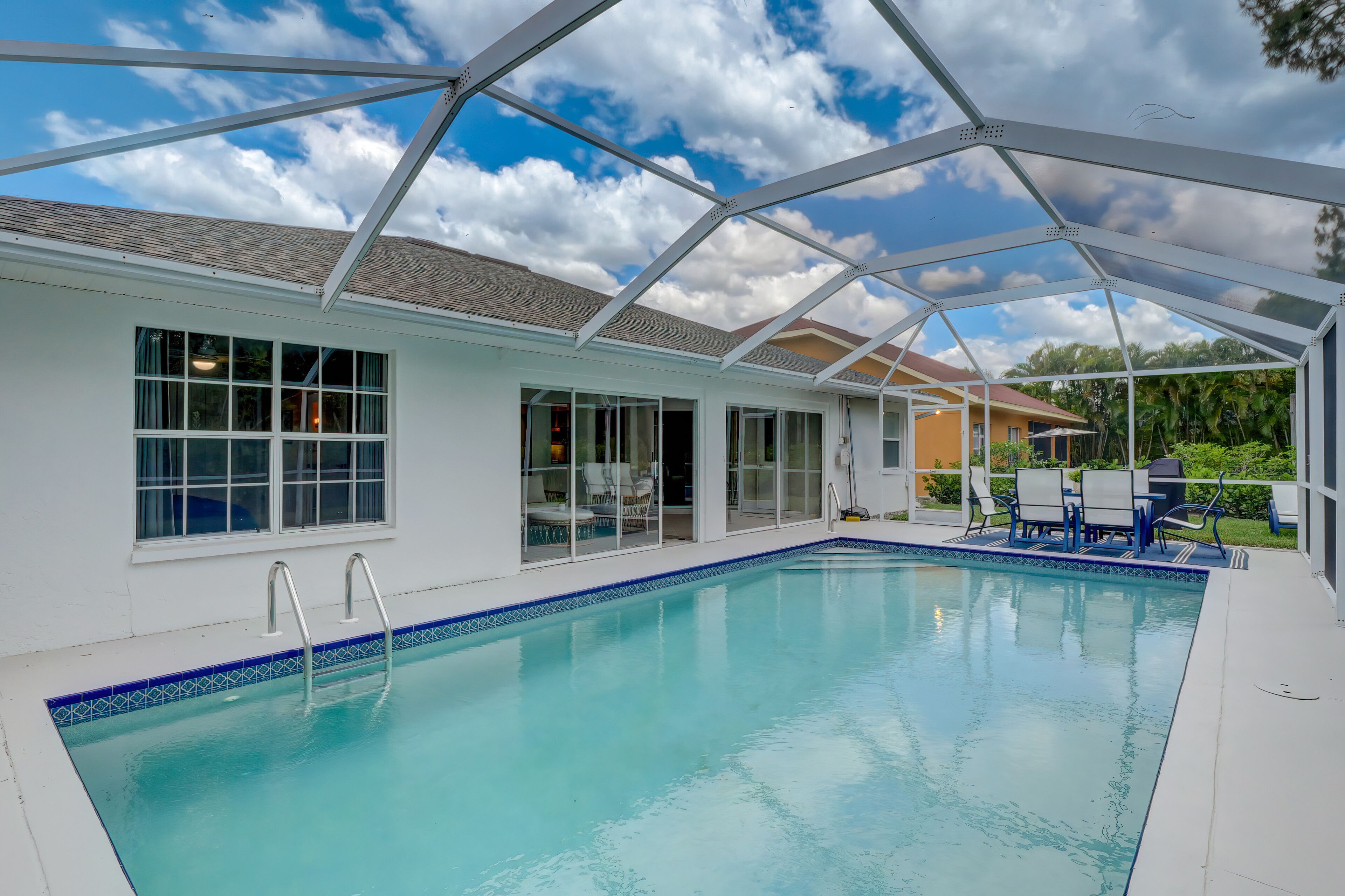 A swimming pool with clear blue water, surrounded by a covered patio area with chairs and tables.