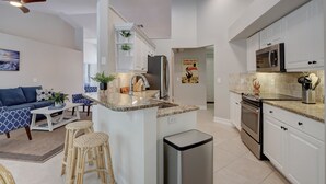 A modern kitchen with white cabinets, a granite countertop, stainless steel appliances, and a small island with stools. - Beautiful Updated Home, Private Pool, Minutes from Downtown 5th Ave & Beaches!!! (Naples)