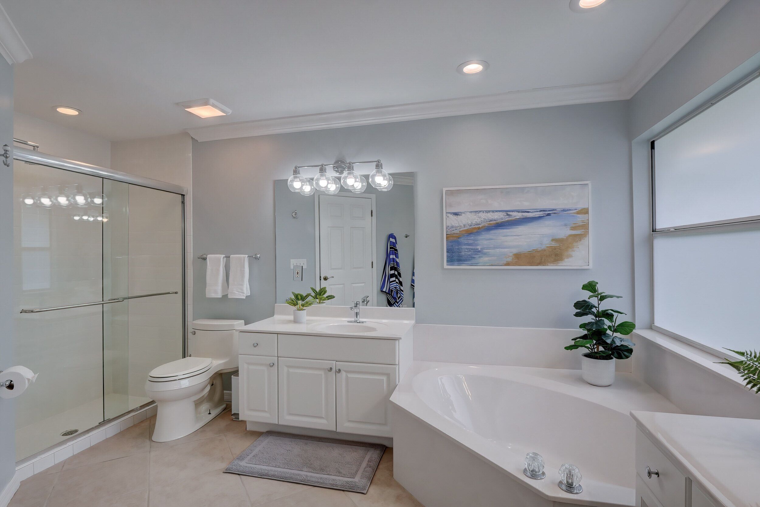 A modern bathroom with a glass shower enclosure, a white toilet, a sink with a mirror, a bathtub, and a potted plant.