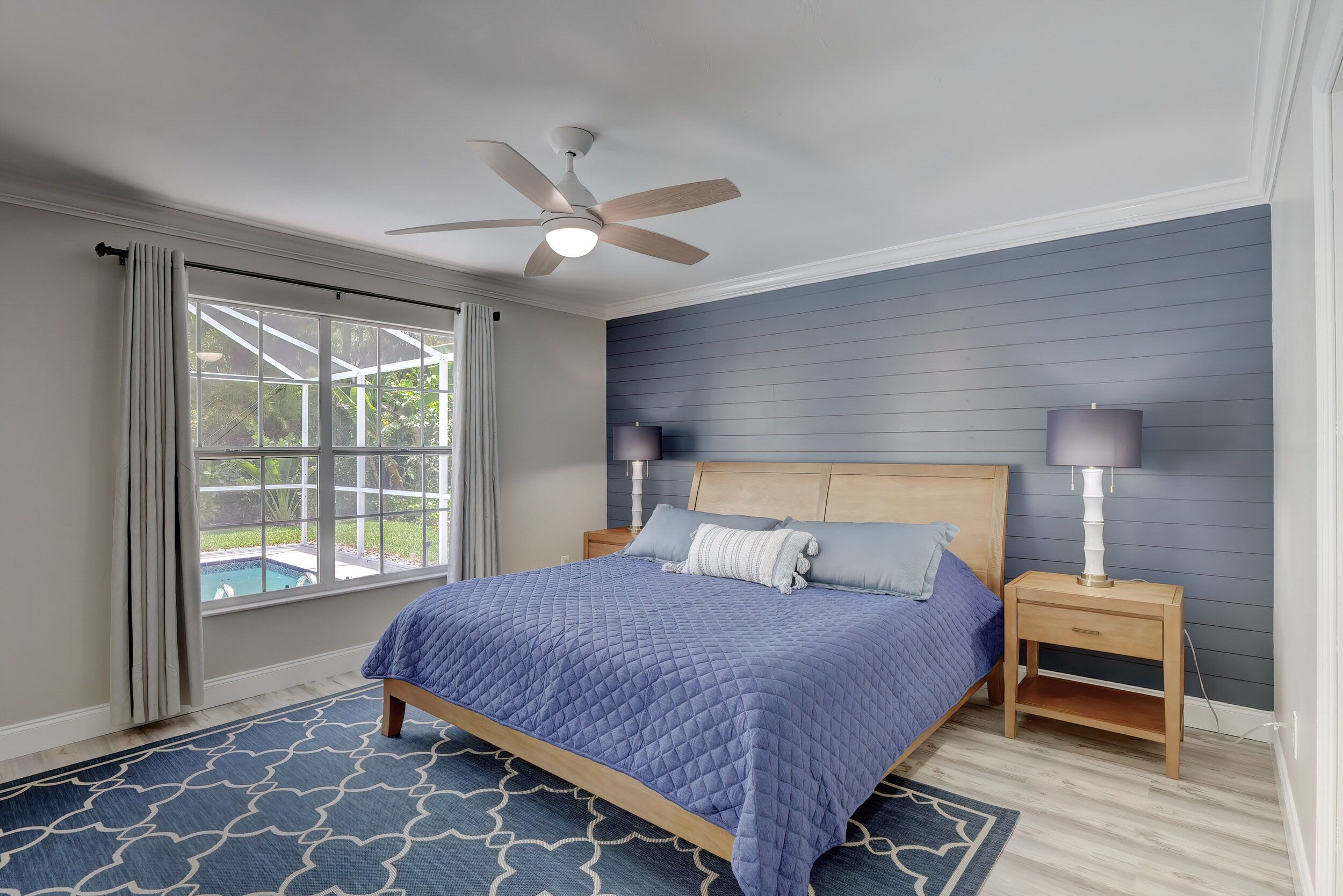 Ein Schlafzimmer mit Bett, Deckenventilator, Nachttischen und Blick auf einen Swimmingpool.