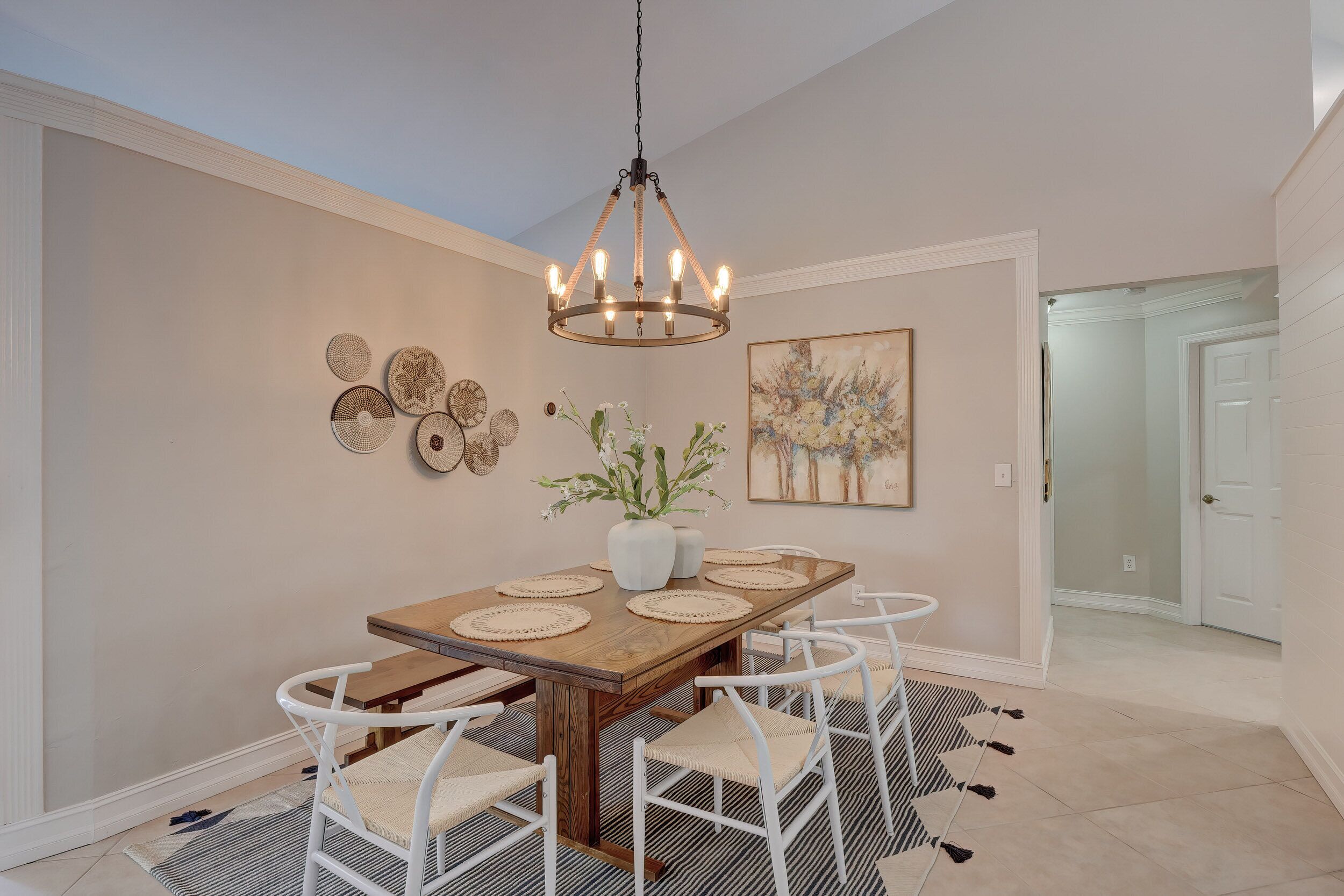 A dining area with a wooden table, white chairs, a chandelier, wall art, and a door in the background.