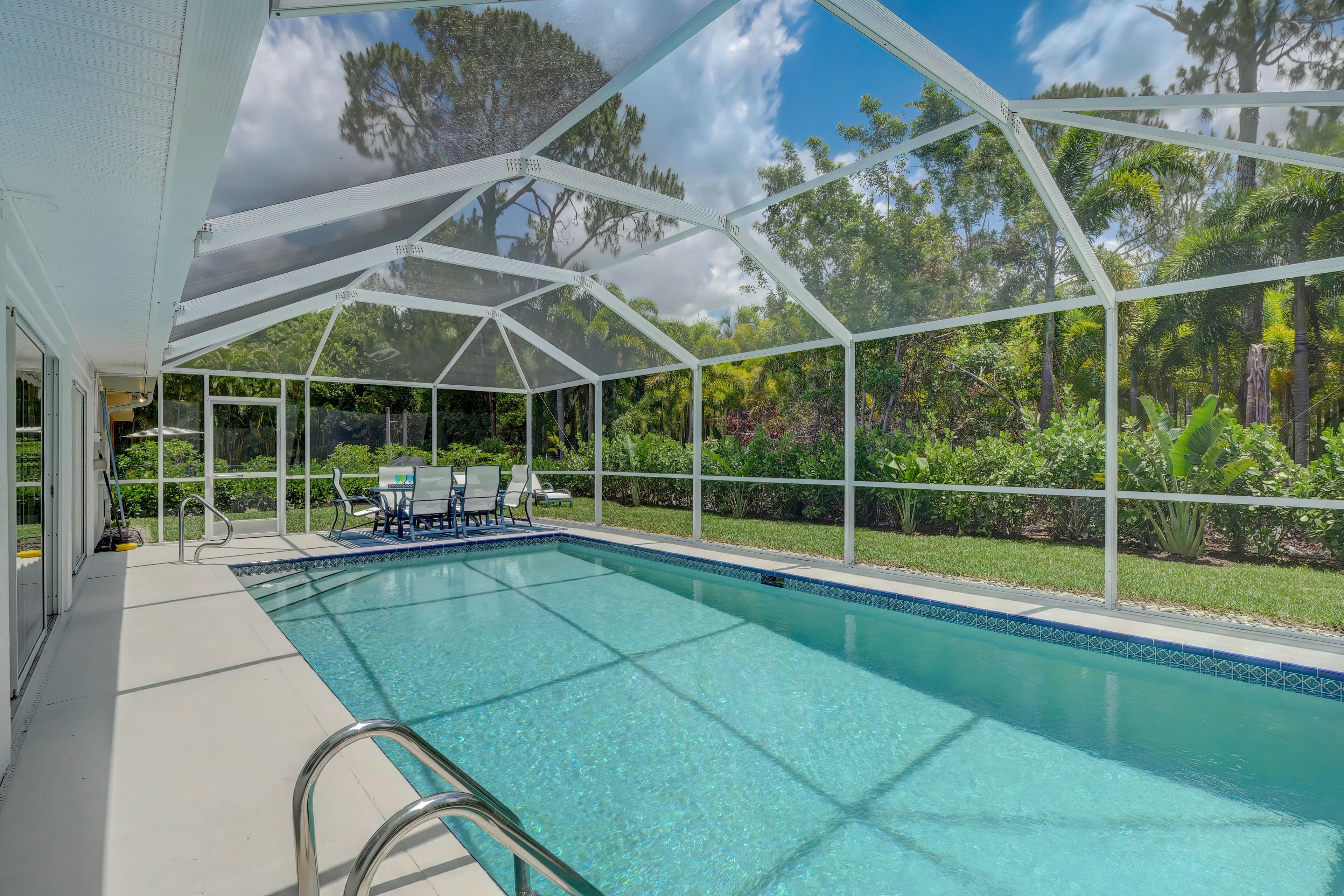 A covered swimming pool with clear blue water, surrounded by lush greenery and trees.