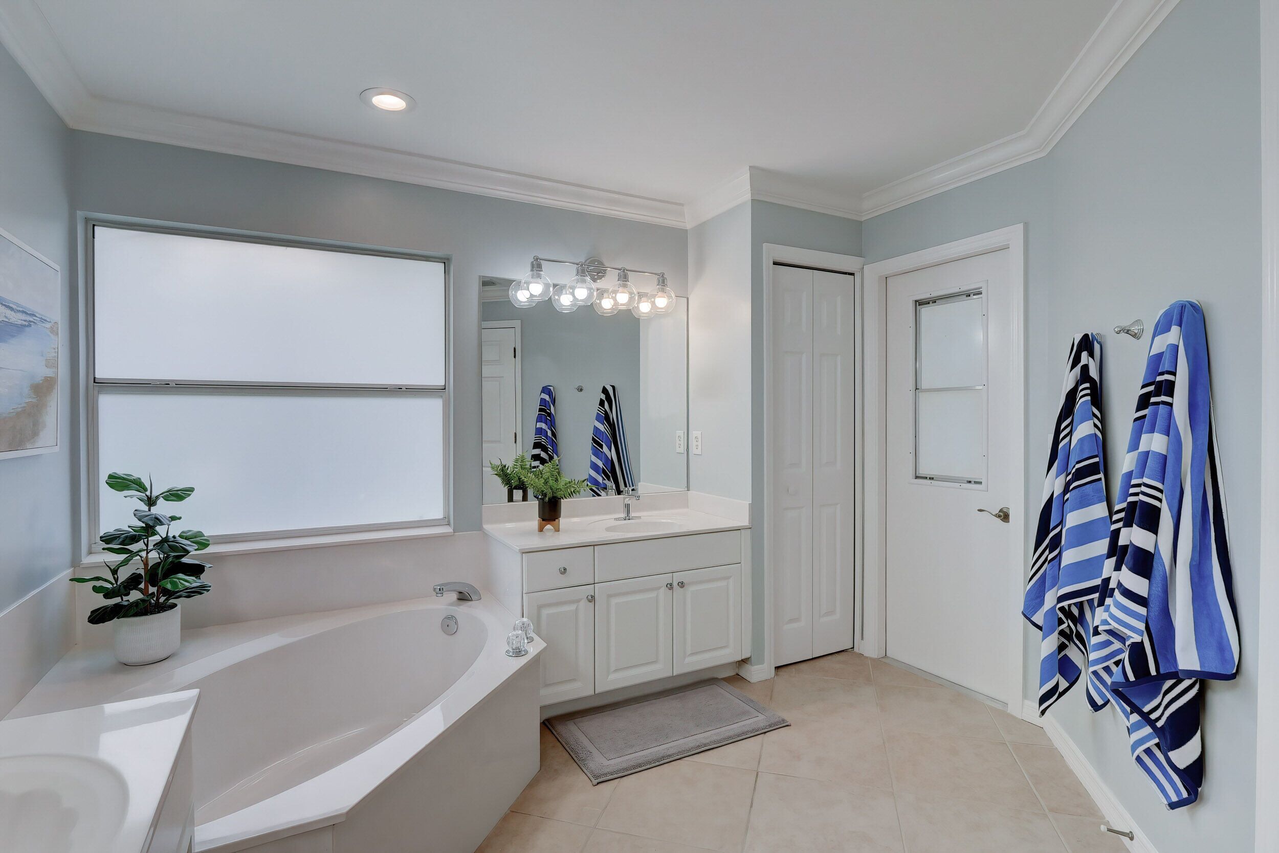 A bathroom with a bathtub, sink, and mirror. There are towels hanging on the wall and a potted plant on the counter.