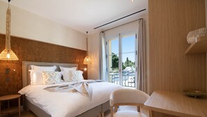 A modern bedroom with a large bed, bedside tables, a chair, a desk, and a view of the outdoors.