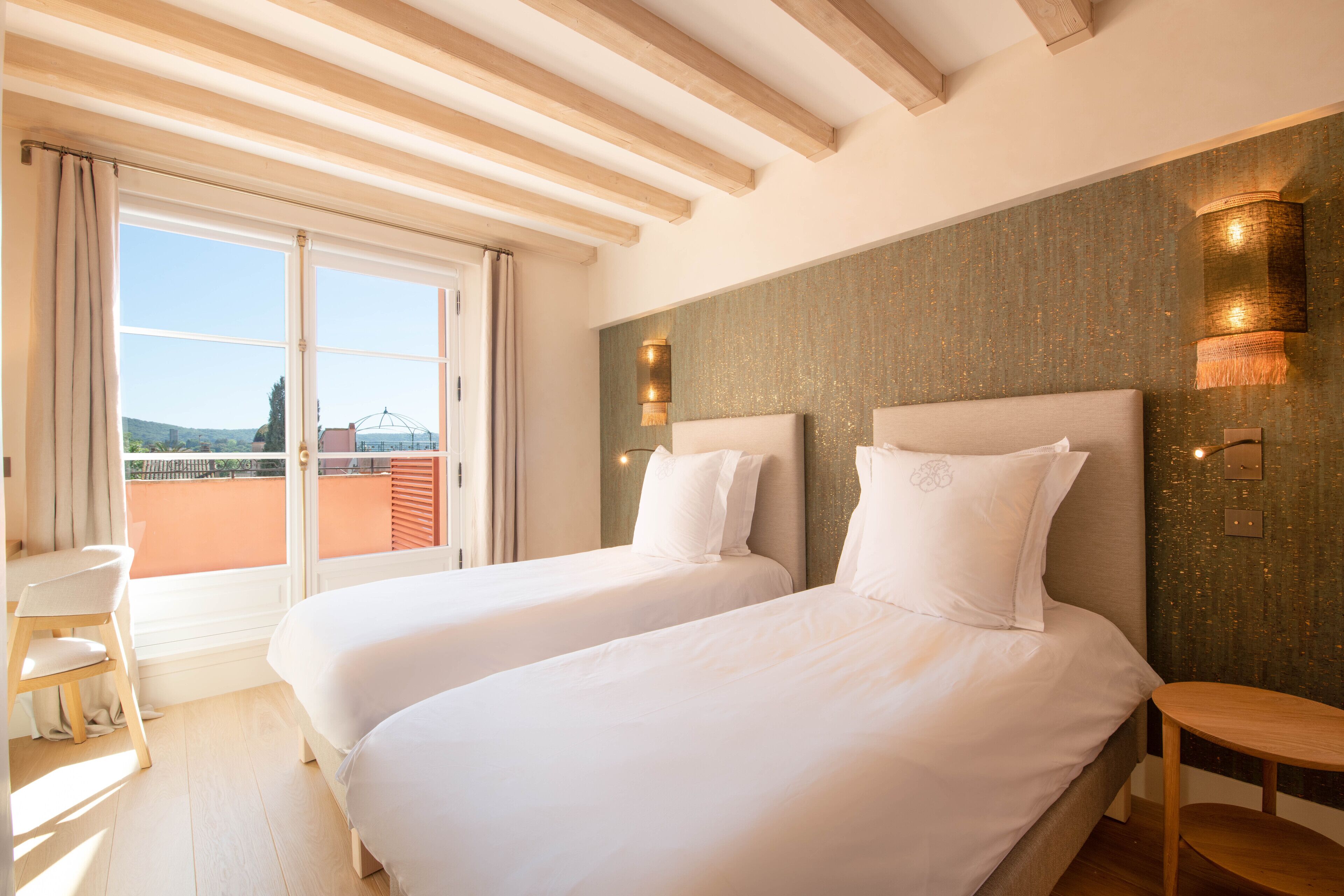 Een hotelkamer met twee bedden, een bureau en uitzicht op de omgeving.