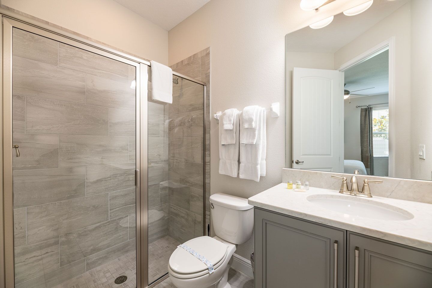 Un baño moderno con cabina de ducha de vidrio, inodoro blanco y tocador con un espejo grande.
