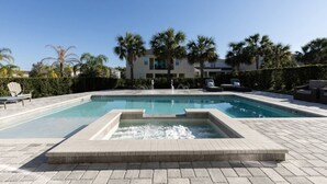 A rectangular swimming pool with a small water feature in the center, surrounded by lounge chairs and a hedge.