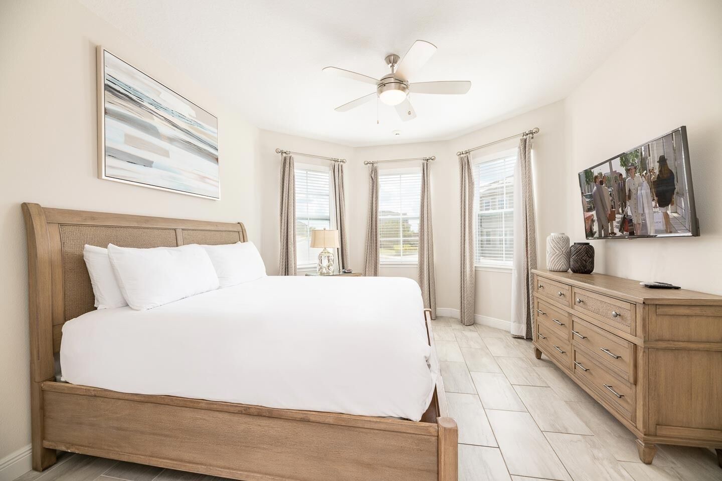 A bedroom with a wooden bed, a ceiling fan, a dresser, and a large window with curtains.