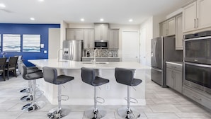A modern kitchen with stainless steel appliances, a central island with bar stools, and a blue accent wall.