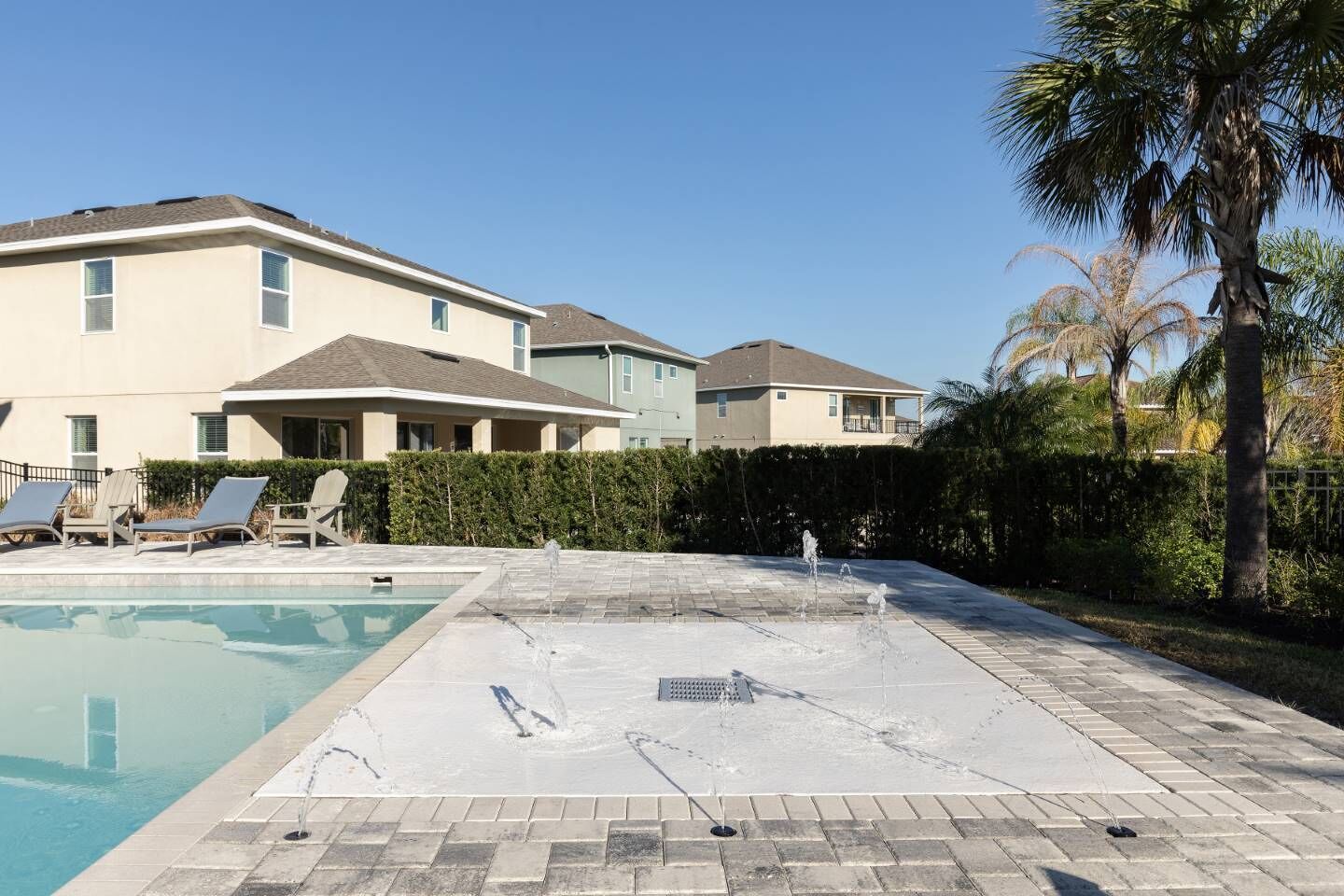 A swimming pool with lounge chairs, a water fountain, and a hedge.