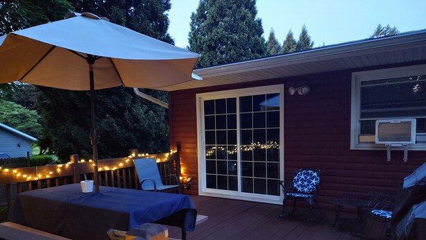 Un terrazzo in legno con tavolo e sedie, luci decorative e un ombrellone grande.