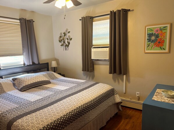 A bedroom with a bed, curtains, an air conditioning unit, a wall-mounted lamp, and a framed floral artwork. - Charming 3 Bedroom Home with Spacious Deck & Boat Parking, near Elk Creek (GIRARD)