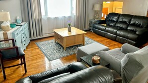 Un soggiorno con un divano in pelle nera, un tavolino in legno, un tappeto decorato e un mobiletti blu.