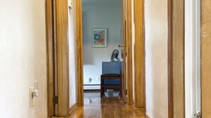 Un corridoio con pavimento in legno, una sedia blu e una ventola su un tavolo.
