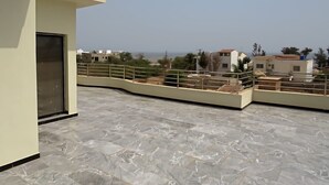 A rooftop terrace with a marble floor, a metal railing, and a view of surrounding buildings.