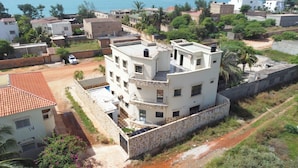 A multi-story residential building with a stone wall, a rooftop terrace, and a view of the sea.