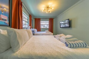 Two beds with white bedding and a geometric-patterned duvet, a flat-screen TV, and a framed picture adorn this stylish room.
