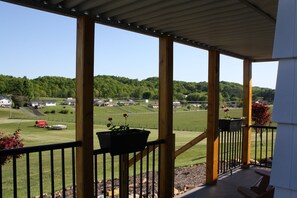 A covered porch with wooden beams and a view of a green landscape.