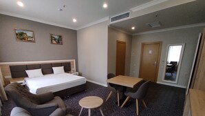 Ein Hotelzimmer mit einem Bett, zwei Sesseln, einem kleinen runden Tisch und einem Esstisch mit Stühlen.