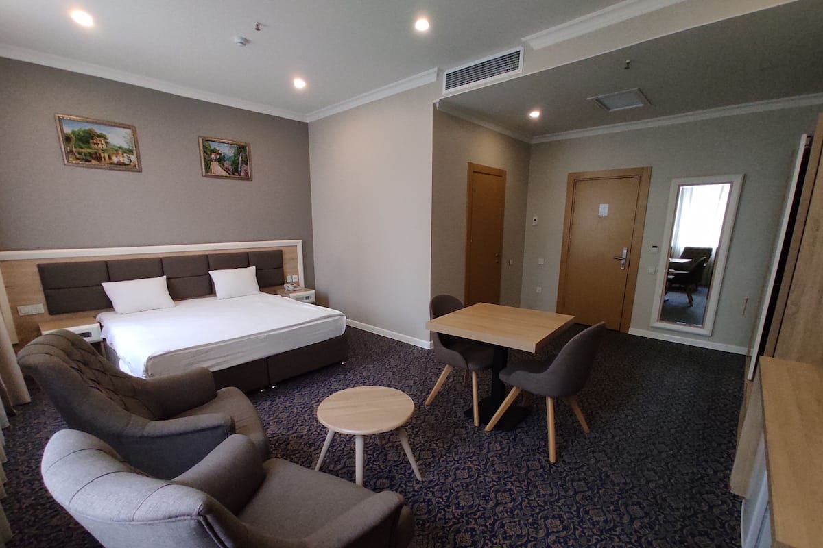 Una habitación de hotel con una cama, dos sillones, una mesita redonda y una mesa de comedor con sillas.