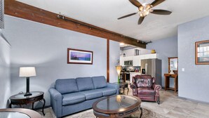 A living room with a blue sofa, a leather armchair, a glass coffee table, and a ceiling fan. - Lovely 1 Bedroom Flat in Downtown Estes Lic#6074 (Estes Park)