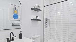 A modern bathroom with a white vanity, a black faucet, a white toilet, and a glass-enclosed shower area.