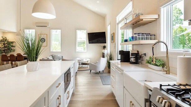 Una cocina moderna con armarios blancos, una isla central, estufa integrada y un comedor con una silla blanca.