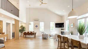 Un amplio y moderno espacio habitable con techo alto, un comedor con mobiliario de madera y una cocina con televisor de pantalla plana.