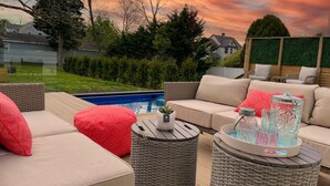 Un espacio al aire libre con piscina, mobiliario de mimbre y vista al atardecer.