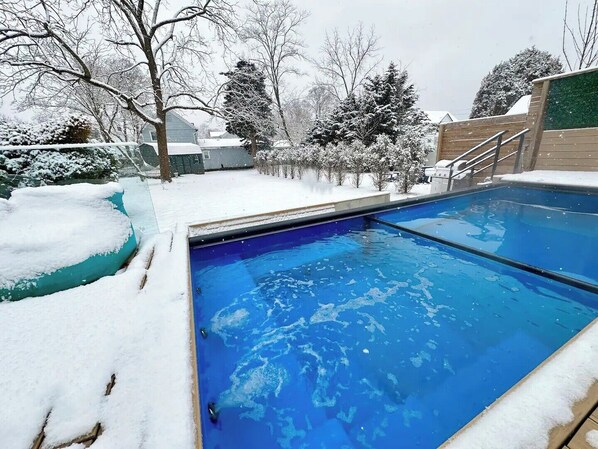 Una piscina con nieve en el borde y árboles circundantes.