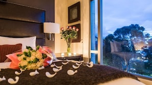 A hotel room with a bed, a nightstand, a vase with flowers, and a view of trees and buildings outside. - Hotel Cabrera Imperial By Key 33 (Bogotá)