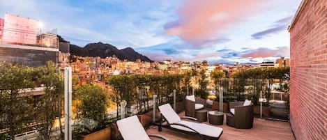 A rooftop terrace with lounge chairs, planters, and a cityscape view.
