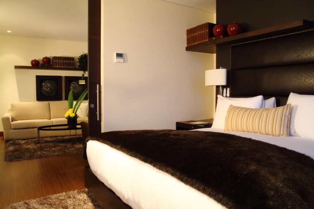 Een moderne hotelkamer met een groot bed, een bank, een salontafel en een boekenkast met decoratieve objecten.