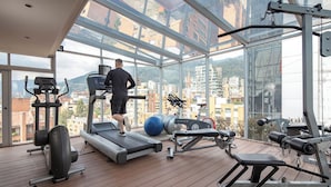 A gym with a treadmill, exercise balls, and weight machines, featuring large windows and a wooden deck. - Hotel Cabrera Imperial By Key 33 (Bogotá)