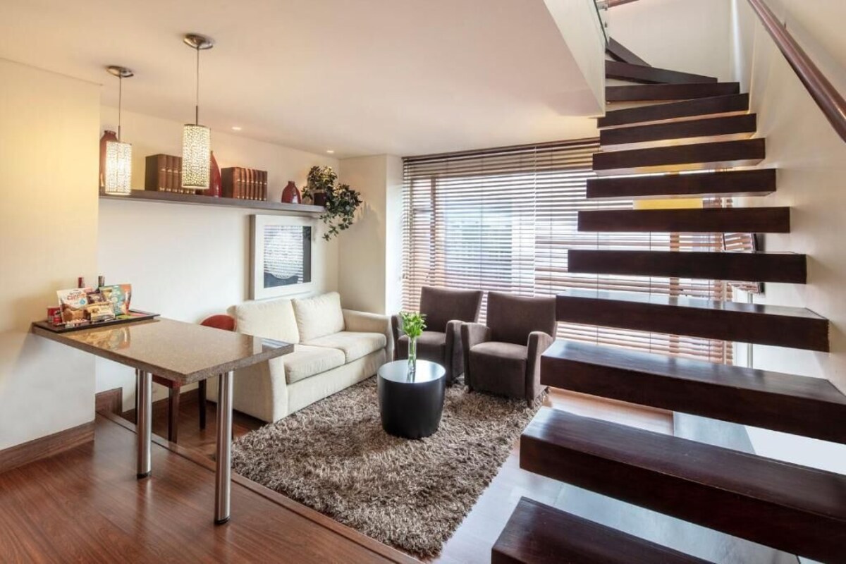 A modern living room with a staircase, a sofa, a coffee table, and a dining area.