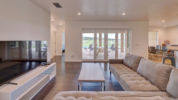 A modern living room with a flat-screen TV, a sofa, a coffee table, and a sliding glass door leading to an outdoor patio. - 1.2 MILE MOTOCROSS TRACK / 4-BED, 3-BA, HEATED POOL HOME  (Fort Pierce)
