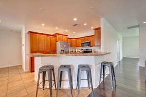 A modern kitchen with wooden cabinets, stainless steel appliances, and a central island with bar stools. - 1.2 MILE MOTOCROSS TRACK / 4-BED, 3-BA, HEATED POOL HOME (Fort Pierce)
